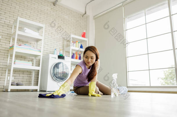 家庭主妇戴着黄色手套，坐在洗衣房地板上，用纤维布，在公寓里喷水，窗灯背景开阔，视野开阔