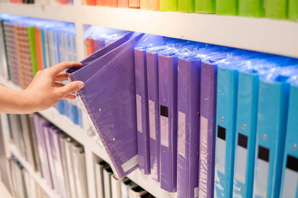 男性手选择新的紫色环活页夹文件夹从五颜六色的货架显示在文具店。购买办公用品概念