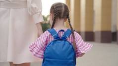 一个带着背包的小孩牵着他妈妈的手去了学校，妈妈带着一个带着书包的小孩绕着校园转，快乐的家庭，一年级的学生，小学的学前教育