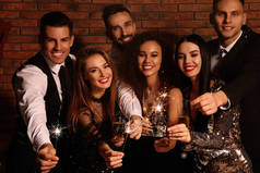 Happy friends with glasses of sparkling wine and sparklers celebrating New Year indoors