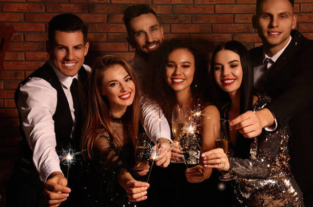 Happy friends with glasses of sparkling wine and sparklers celebrating New Year indoors