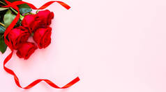 粉色背景上的红玫瑰。爱忏悔。情人节的庆祝活动。红玫瑰和彩带，情人节的概念，周年纪念日，母亲节和生日问候，复制空间，顶视图.
