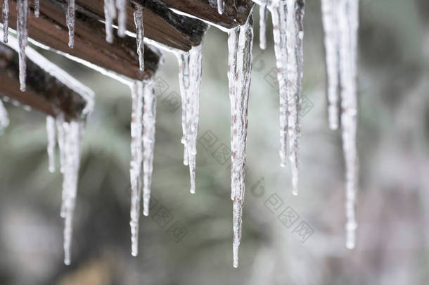 冬天结束时屋顶上的冰柱.融化，融化的冰雪在春天。屋顶上的<strong>水滴</strong>缓缓<strong>落下</strong>.模糊的背景和错误h.