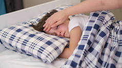 有爱心的母亲把头靠在生病的儿子额头上。儿童保健概念。可怜的小男孩躺在床上.