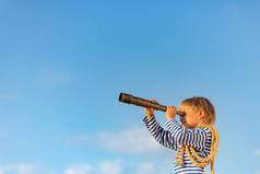 快乐的孩子在蓝天的映衬下透过老式的望远镜观看.夏天玩得开心的孩子。想象力和自由的概念.
