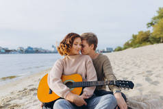 年轻人教他的女朋友弹吉他，自学。情侣们在海滩上拥抱亲吻，享受快乐