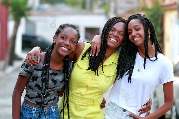 Casual <strong>happy</strong> mother and teen daughters standing outside. Authentic interaction. African ethnicity