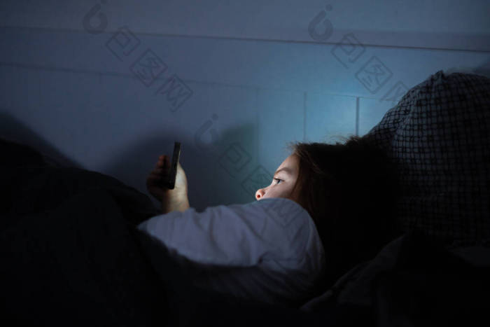 小女孩晚上睡觉前在床上看智能手机上的视频图片-包图网企业站
