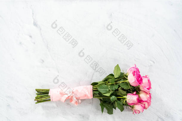 粉红玫瑰花束，用粉红包装纸包裹，混凝土背景上有粉红缎带.
