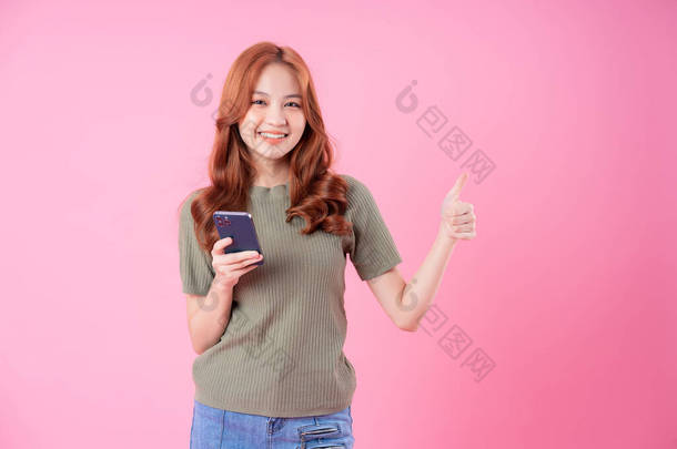 在粉红背景下使用智能<strong>手机</strong>的年轻亚洲<strong>女性</strong>