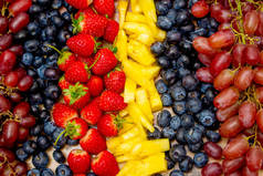 新鲜水果背景，排列成一排葡萄、各种浆果和菠萝片.