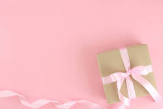 褐色纸制礼品盒，粉红缎子卷丝带蝴蝶结在粉红的背景上。平铺母亲节、父亲节、情人节、带有复制空间的生日观念.
