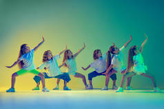 同步移动。一群孩子，穿着运动型休闲装的小女孩在舞蹈班里跳着舞，在霓虹灯下与绿色背景隔离。音乐、时尚、艺术的概念