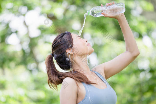 在夏天的绿色公园里，年轻美丽的女运动员在脸上不停地喝水和泼水，女运动员在运动后从塑料瓶里喝水