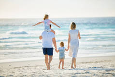 快乐的一家人在海滩上散步。带着孩子度假开心的年轻父母的后视镜。小男孩和小女孩和爸爸妈妈一起享受夏天.