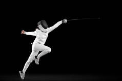 Energetic female fencer in white fencing costume and mask in action, motion isolated on dark backgro