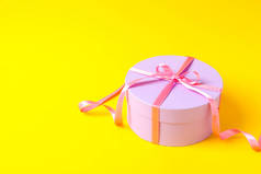 Round gift box with bow on yellow background