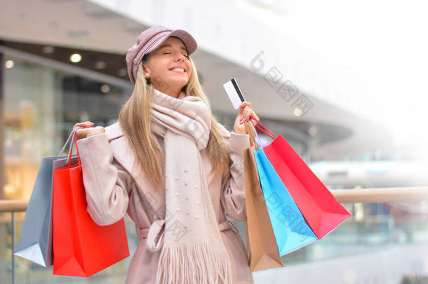 在商场里，带着信用卡和购物袋的美丽而快乐的年轻女子的画像。销售。网上购物中心，星期一，黑色星期五