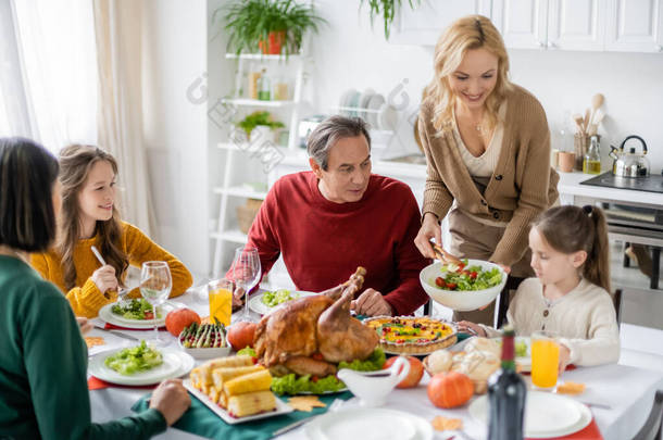 <strong>感恩节大</strong>餐期间，在女儿和家人身边放沙拉的笑女人