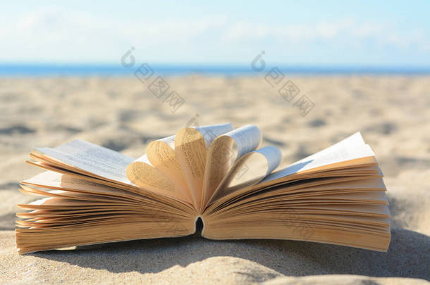 Open book on sandy beach near sea
