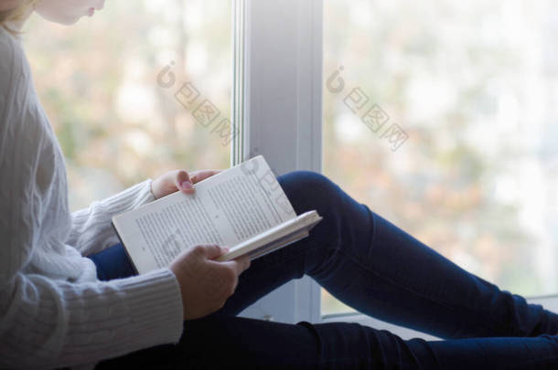 一个穿着白色羊毛衫的女人拿着一本书的近景。为您模拟阅<strong>读书籍</strong>的概念背景腾出的空间.