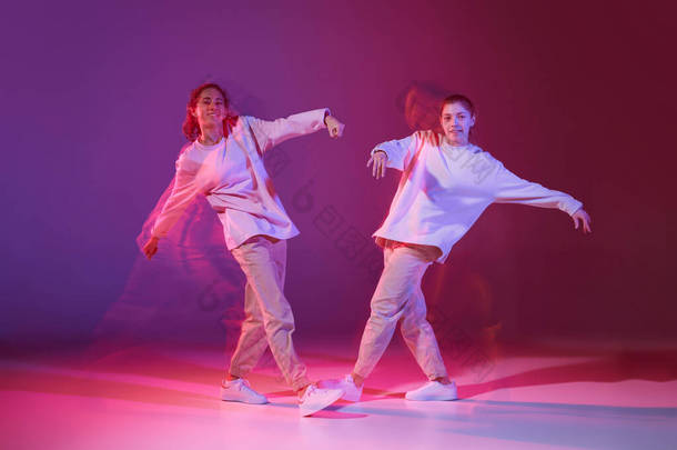 两个年轻女孩在霓虹灯下在深紫色<strong>背景</strong>上跳嘻哈舞的肖像。随便看看。运动概念、青年文化、积极的生活方式、行动、街头<strong>舞蹈</strong>