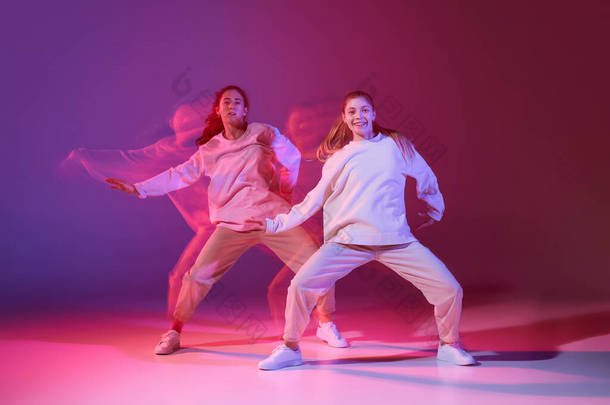 两个年轻女孩在霓虹灯下在深紫色背景上跳嘻哈舞的肖像。现代风格。运动概念、青年文化、积极的生活方式、行动、街头舞蹈