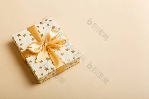 用白色的纸包裹着圣诞节或其他节日手工制作的礼物，背景为金色缎带。礼品盒，彩色桌上的礼品装饰，顶部有复印空间.