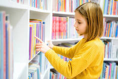女学生在学校图书馆选书.聪明的女孩选择阅读的文献。书店架子上的书。从书本中学习。学校教育。日常阅读的益处