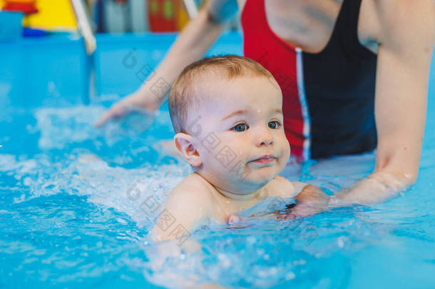 一位游泳老师教一个小男孩在游泳池里游泳。孩子们的第一个游泳课。婴儿发育