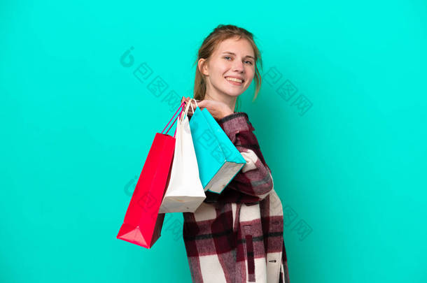 Young English woman isolated on blue background holding <strong>shopping</strong> bags and smiling