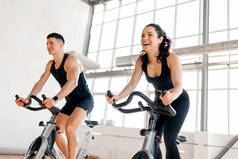 beautiful athletic couple of cyclists train in the fitness room on static bicycle simulator, man tra