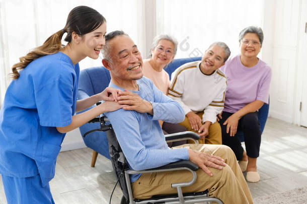 护理治疗师与坐在轮椅上的一位亚洲老年人站在一起，后面是一群坐在沙发上的老年妇女。疗养院为一个支助小组提供便利.