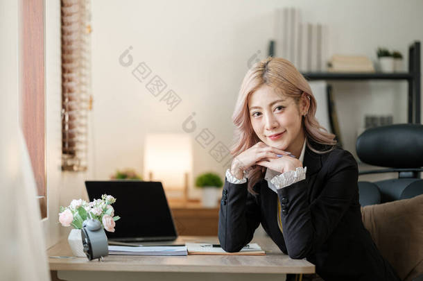 在办公室的笔记本电脑上，身穿正式西服的亚洲漂亮女商人在工作场所工作。迷人的女<strong>员工</strong>办公室职员笑了。高质量的<strong>照片</strong>