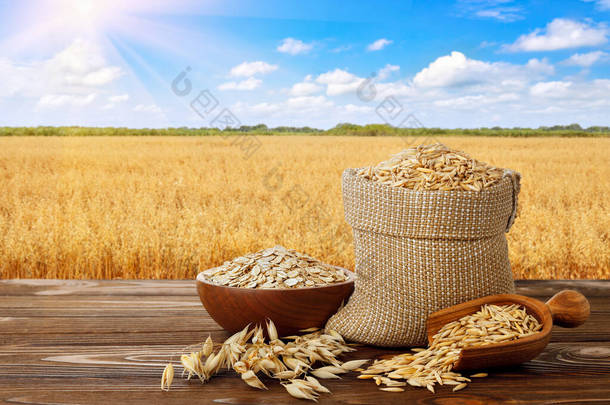 未煮熟的燕麦片放在碗里，燕麦谷粒放在背包里放在桌子上，背景是成熟的麦田
