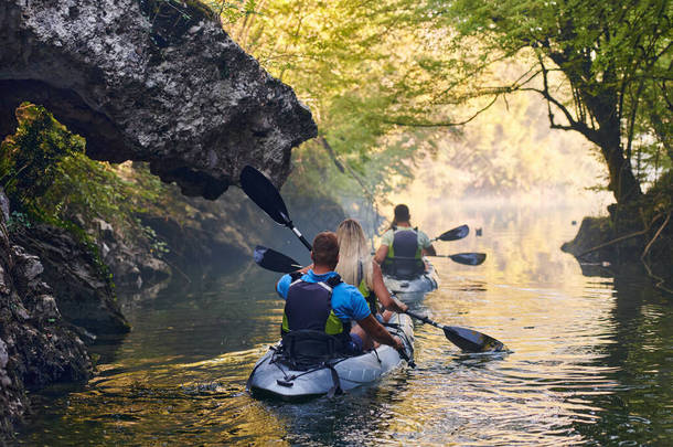 一群朋友在平静的河流、周围的森林和大峡谷中畅游，一边玩一边划皮划艇.