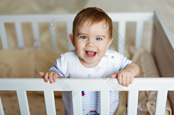 <strong>小可爱小可爱</strong>金发的男孩，在条纹的大包围是在育儿室，白色的婴儿床和笑