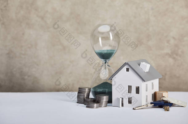 房子模型在白色桌子上与沙漏,硬币和钥匙,房地产概念