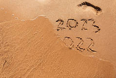 再见2022年新年快乐2023在阳光明媚的日子里，在海滩上挥洒着海浪和清澈的大海。在美丽的金色沙滩上手写2022年和2023年的题词。2023年新年取代2022年概念