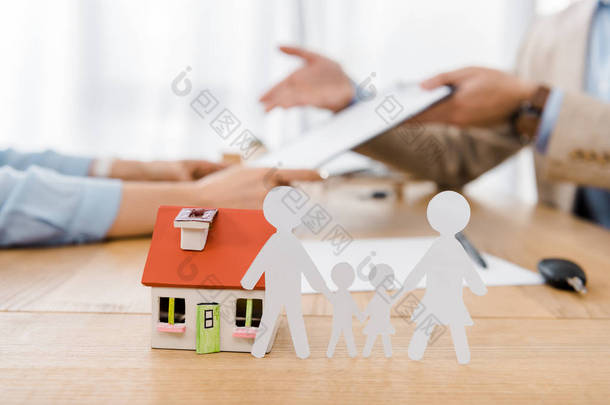 白皮书在背景、生活和房屋保险方面模糊的人在木桌上剪下了家庭和<strong>房屋模型</strong>