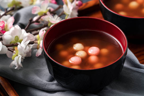 用红白相间的汤圆（汤圆，糯米饺子球）和甜糖浆汤盛在蓝色桌旁的碗里，准备过冬.
