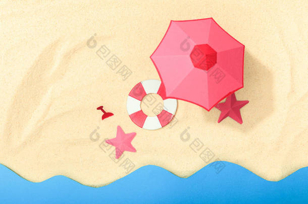 在靠近海洋的纹理沙滩上，有救生圈、粉红色雨伞和海星的纸海滩顶视图