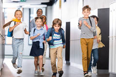 兴奋的多文化学生与背景教师沿着学校走廊奔跑