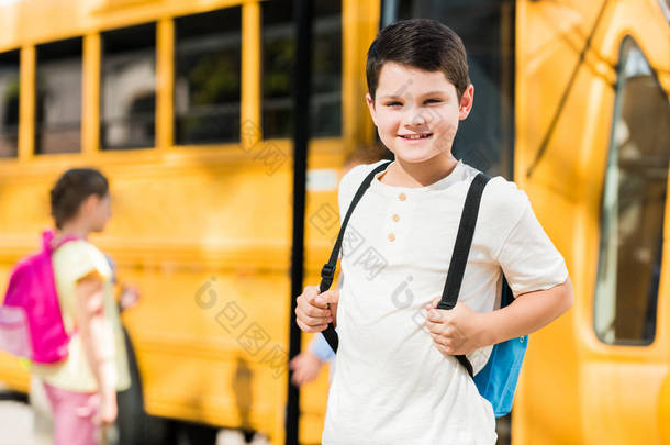 快乐的小男孩背包站在校车前