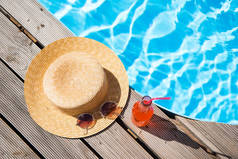 顶部视图的柳条帽, 太阳镜和瓶子在游泳池附近的夏日饮料