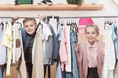 两个微笑的孩子看着相机, 而站在布衣架在商店