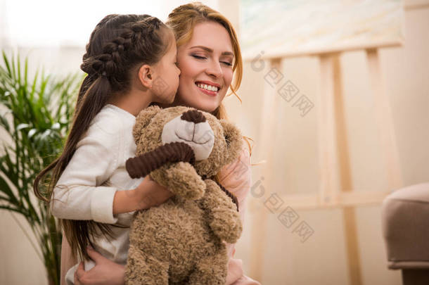 可爱的小<strong>孩子抱</strong>着泰迪熊和亲吻快乐的<strong>母亲</strong>在家