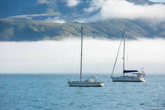 在Akaroa港，蓝天，白云，雾气和海水。在新西兰坎特伯雷Akaroa港口一带的渔船和帆船也得到了支持。.