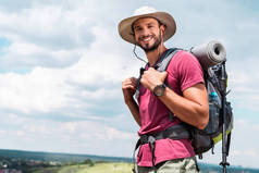 微笑的旅行者在帽子与背包和旅游垫看照相机