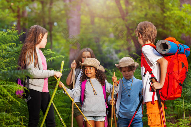 一群<strong>小孩</strong>子在徒步旅行的路上互相交谈在森林里用杆子和背包<strong>走路</strong>